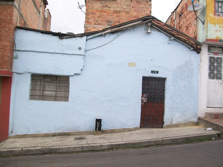 the house is painted a light sky blue, and is sandwiched between two larger buildings